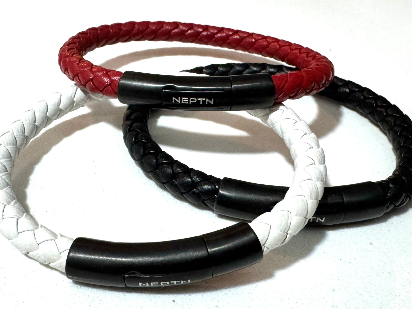 Three braided leather bracelets in red, black, and white with black clasp on a white background.